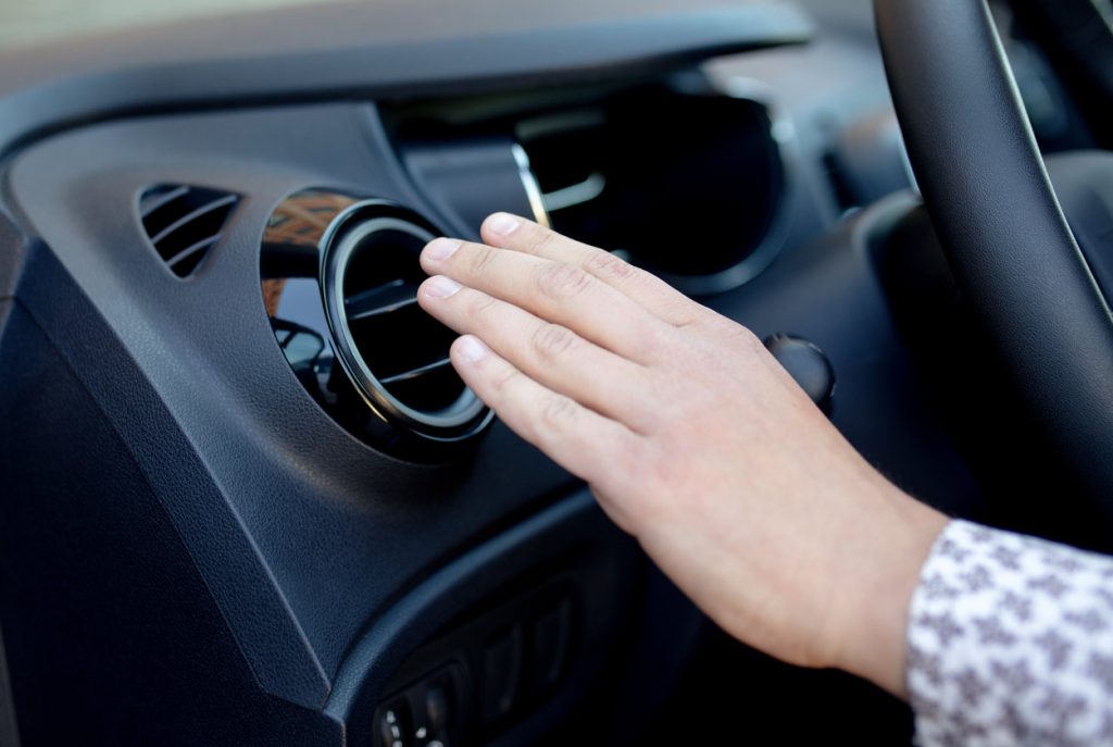 person holding hand over car air conditioner 