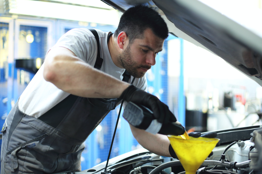 man pouring oil into funnel on car engine